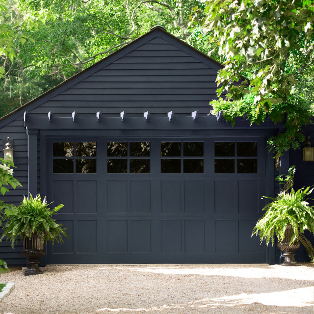 A rich navy blue-painted garage is surrounded by lush greenery. A rich navy blue-painted garage is surrounded by lush greenery.