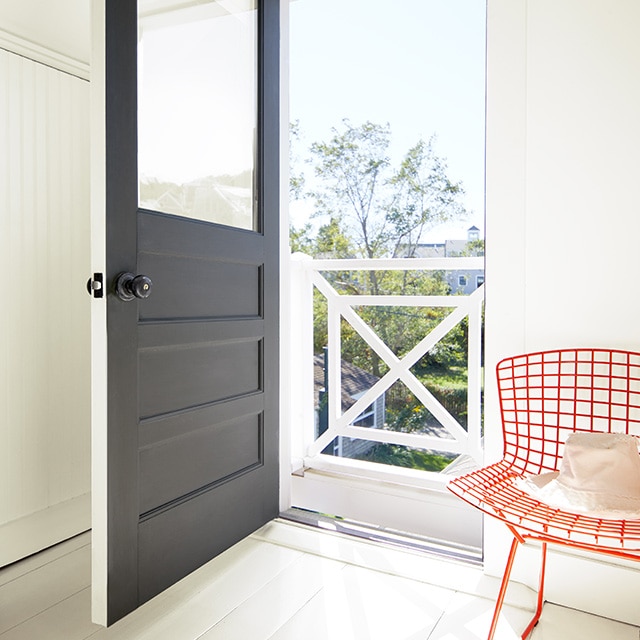 An entryway to a home with white-painted walls features an open black-painted door and a red, metal chair. An entryway to a home with white-painted walls features an open black-painted door and a red, metal chair.