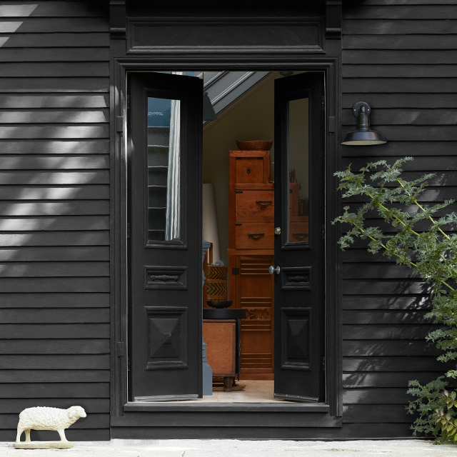 A black-painted home exterior, with open, black-painted front doors and trim, and a small decorative lamb statue. A black-painted home exterior, with open, black-painted front doors and trim, and a small decorative lamb statue.
