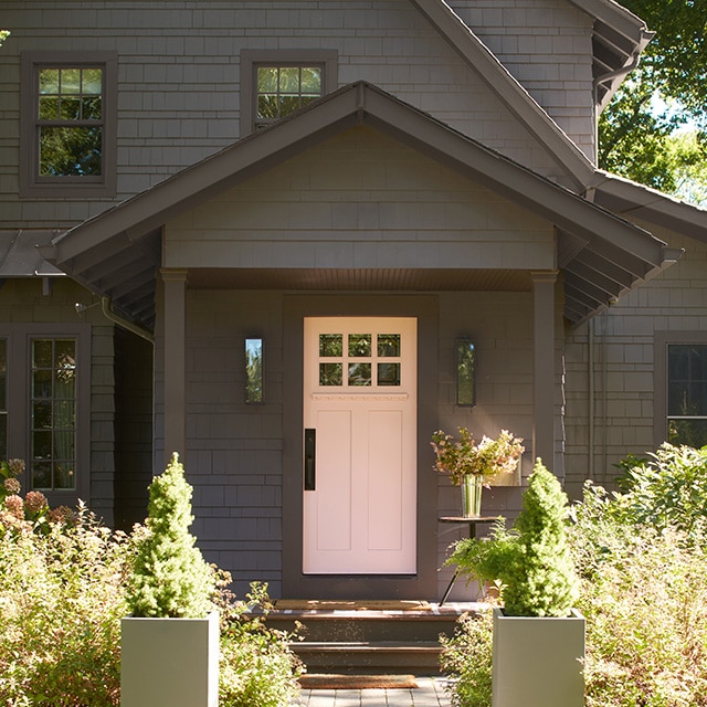 A soothing pink-painted front door makes a lovely contrast on this soft black-painted house, nestled among trees and front shrubs. A soothing pink-painted front door makes a lovely contrast on this soft black-painted house, nestled among trees and front shrubs.