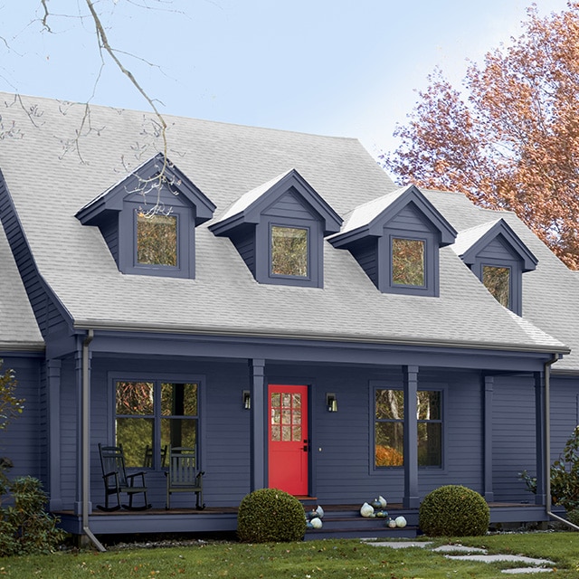 A beautiful navy blue painted Cape Cod style home features dormer windows, a front porch with pillars, and a striking red painted front door. A beautiful navy blue painted Cape Cod style home features dormer windows, a front porch with pillars, and a striking red painted front door.