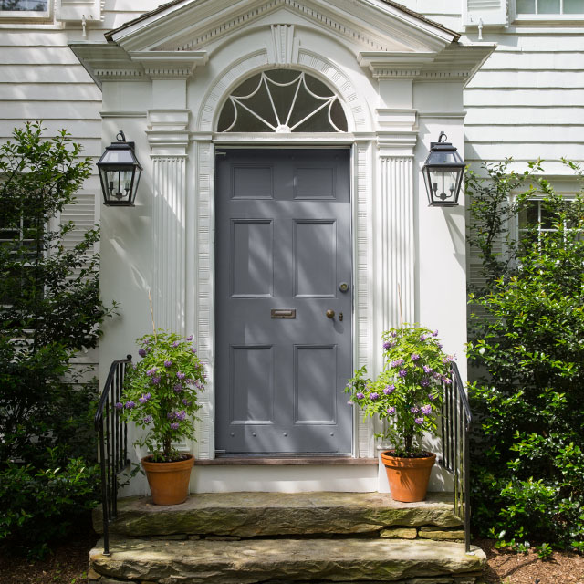 A colonial-style home front entrance with a gray painted door, white exterior, and stone steps. A colonial-style home front entrance with a gray painted door, white exterior, and stone steps.