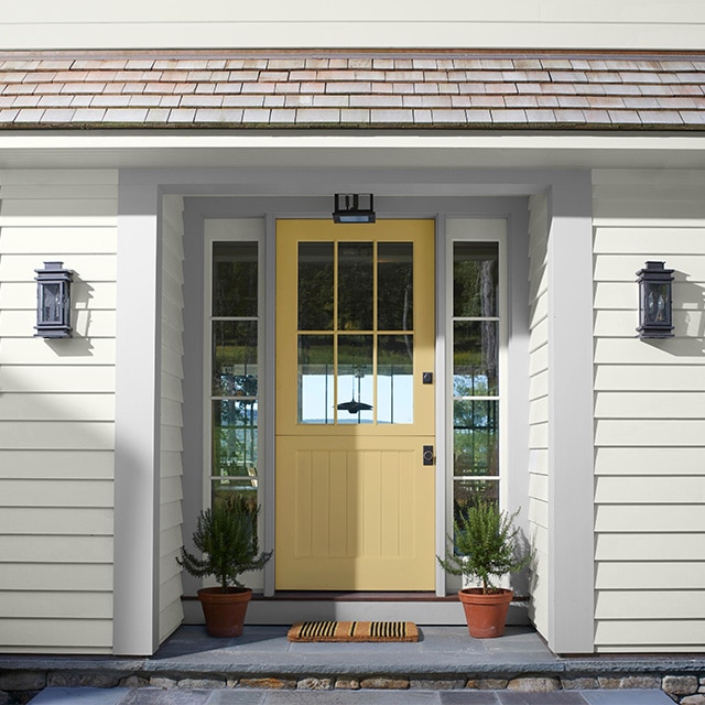A white-painted house with a pretty yellow-gold front door, light gray trim, and a small shingled roof over the door and two small windows. A white-painted house with a pretty yellow-gold front door, light gray trim, and a small shingled roof over the door and two small windows.