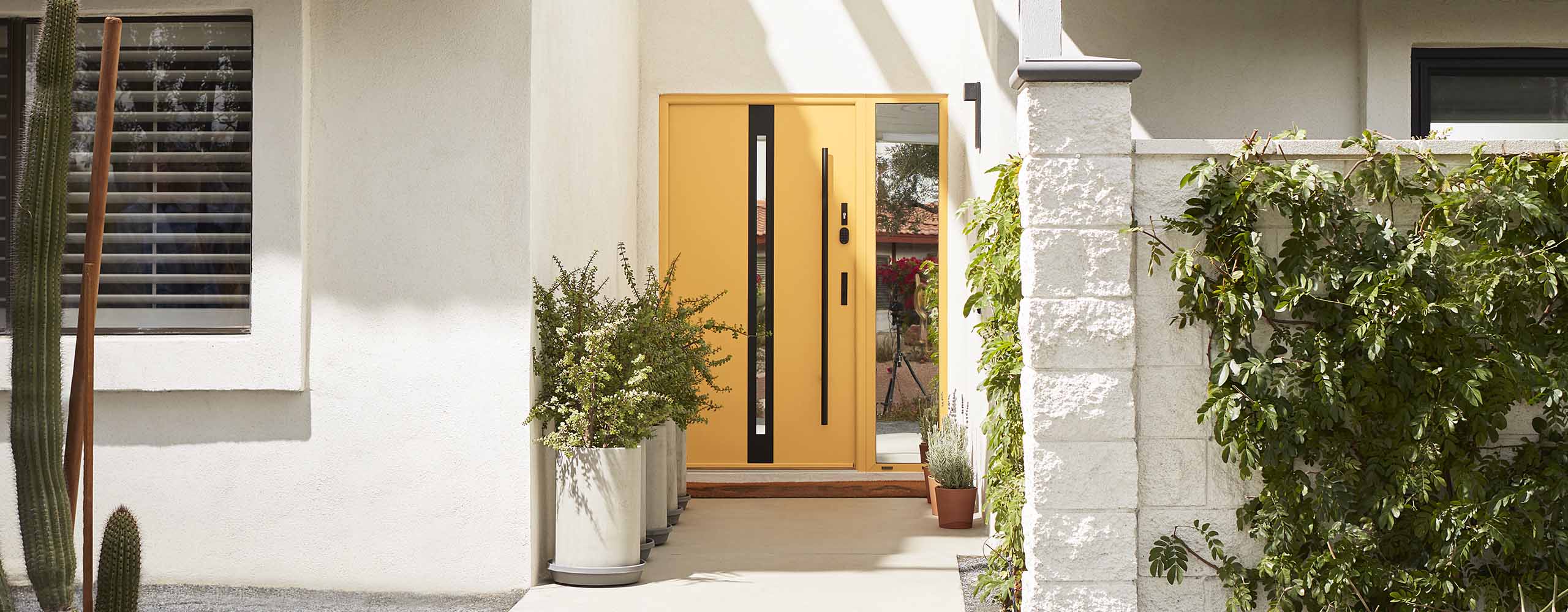 A white-painted stucco home exterior with a pretty yellow front door, a white tiled roof, and potted plants on the front walkway. A white-painted stucco home exterior with a pretty yellow front door, a white tiled roof, and potted plants on the front walkway.