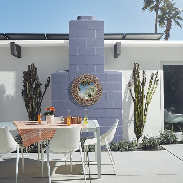 A white-painted stucco home with a light purple chimney flanked by two cacti creates a fun outdoor space to this patio with white dining furniture. A white-painted stucco home with a light purple chimney flanked by two cacti creates a fun outdoor space to this patio with white dining furniture.