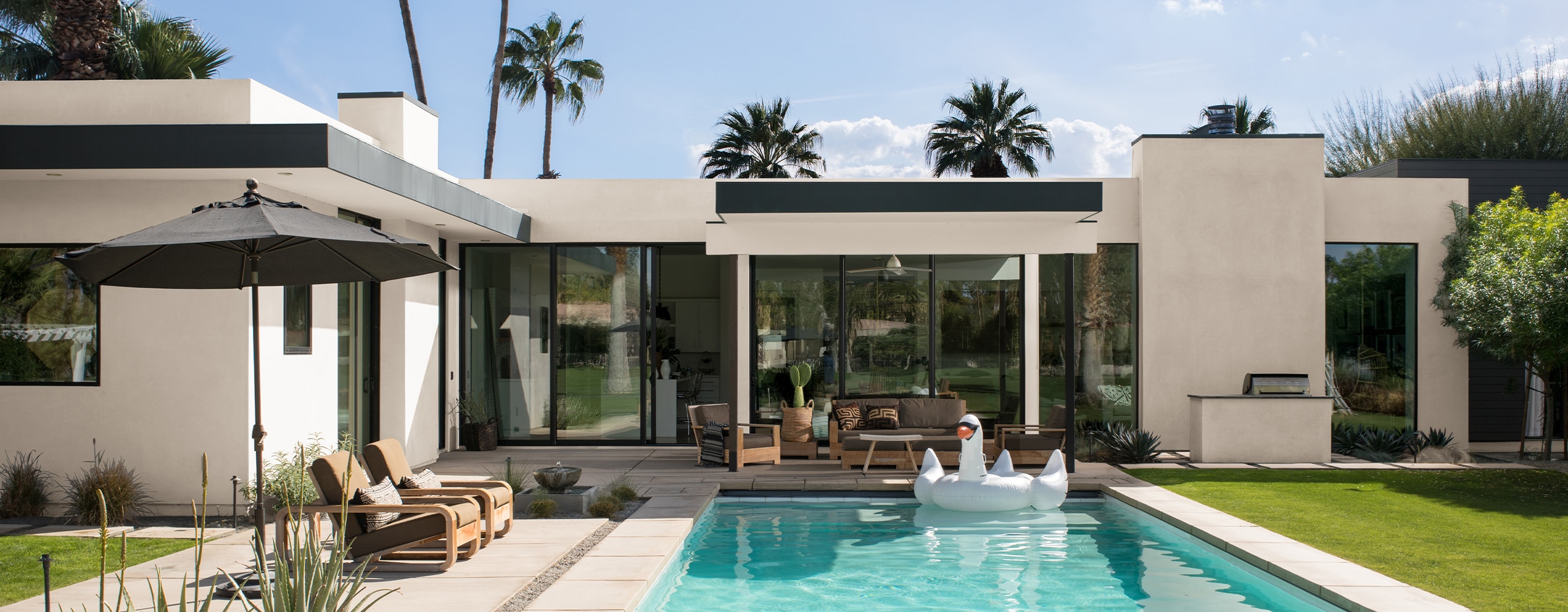 A modern, white-painted stucco house with black trim and palm trees features a beautiful backyard pool and patio. A modern, white-painted stucco house with black trim and palm trees features a beautiful backyard pool and patio.