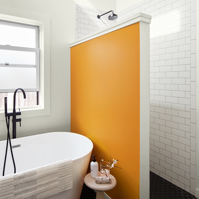 A fun, orange-painted accent wall separates the walk-in shower from a free-standing bathtub in a white painted bathroom with white subway tile. A fun, orange-painted accent wall separates the walk-in shower from a free-standing bathtub in a white painted bathroom with white subway tile.