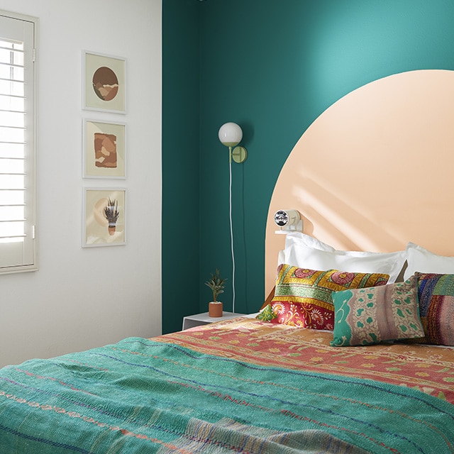 A white bedroom with a teal green-painted accent wall and peach painted arch behind a bed with teal and orange bohemian style bedding and pillows. A white bedroom with a teal green-painted accent wall and peach painted arch behind a bed with teal and orange bohemian style bedding and pillows.