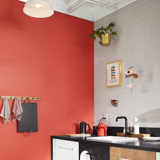 A sleek kitchen corner with a coral painted wall, a white tiled backsplash wall and floor, white upper wall and exposed pipes, and three sets of drawers: one painted white, the second black, and the third woodgrain. A sleek kitchen corner with a coral painted wall, a white tiled backsplash wall and floor, white upper wall and exposed pipes, and three sets of drawers: one painted white, the second black, and the third woodgrain.