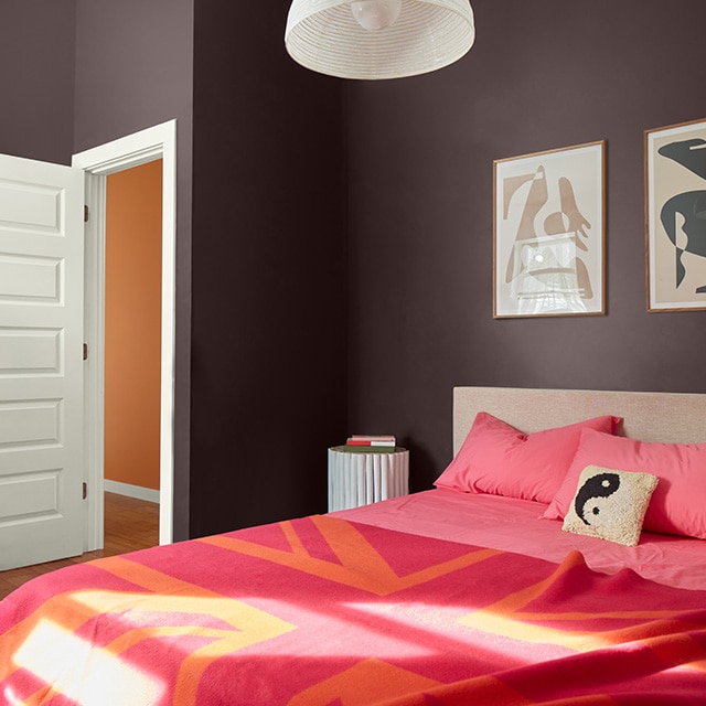 Bright orange and red print bedding contrast nicely in this chocolate brown painted bedroom with white trim and an open white door, revealing an orange painted hallway wall. Bright orange and red print bedding contrast nicely in this chocolate brown painted bedroom with white trim and an open white door, revealing an orange painted hallway wall.