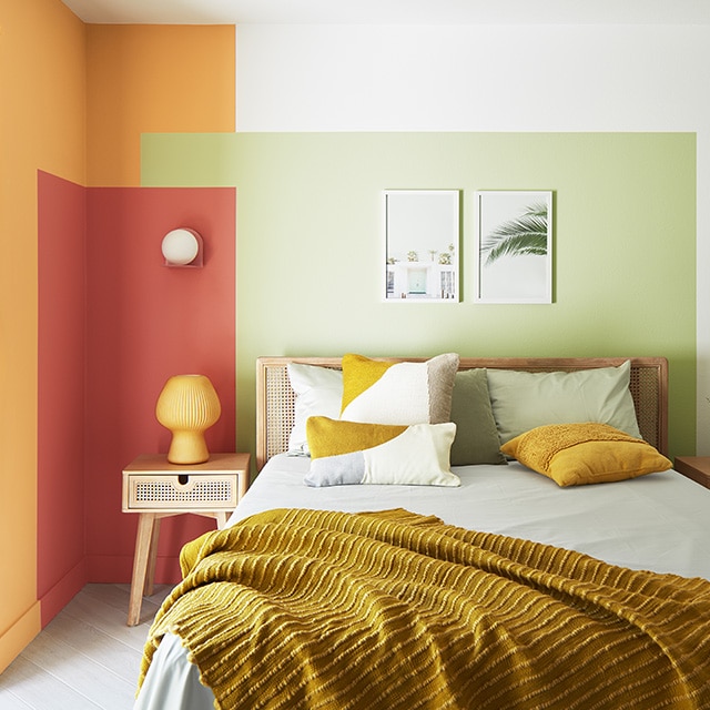 A cheerful corner bedroom space with golden yellow, orange, and green painted overlapping rectangles on a white wall behind a modern bed and night stands. A cheerful corner bedroom space with golden yellow, orange, and green painted overlapping rectangles on a white wall behind a modern bed and night stands.