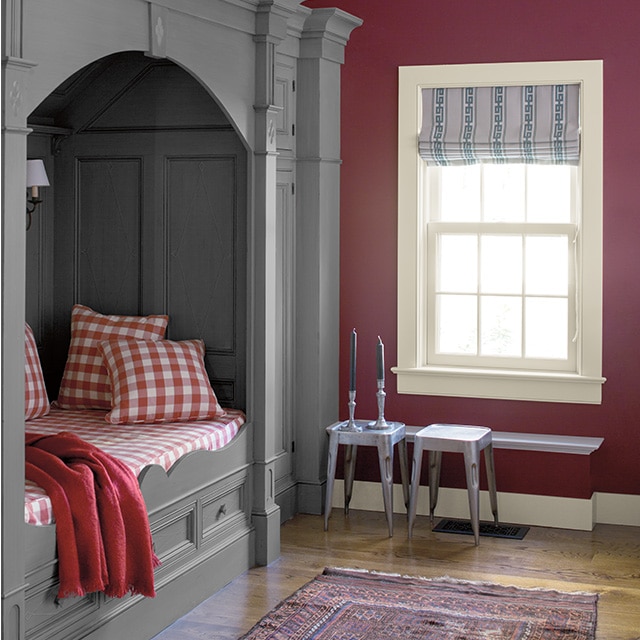 A gray-painted alcove bed with paneled inner walls, elegant molding and red checkered bedding creates a cozy nook in a plum painted bedroom with a white trimmed window and ceiling. A gray-painted alcove bed with paneled inner walls, elegant molding and red checkered bedding creates a cozy nook in a plum painted bedroom with a white trimmed window and ceiling.