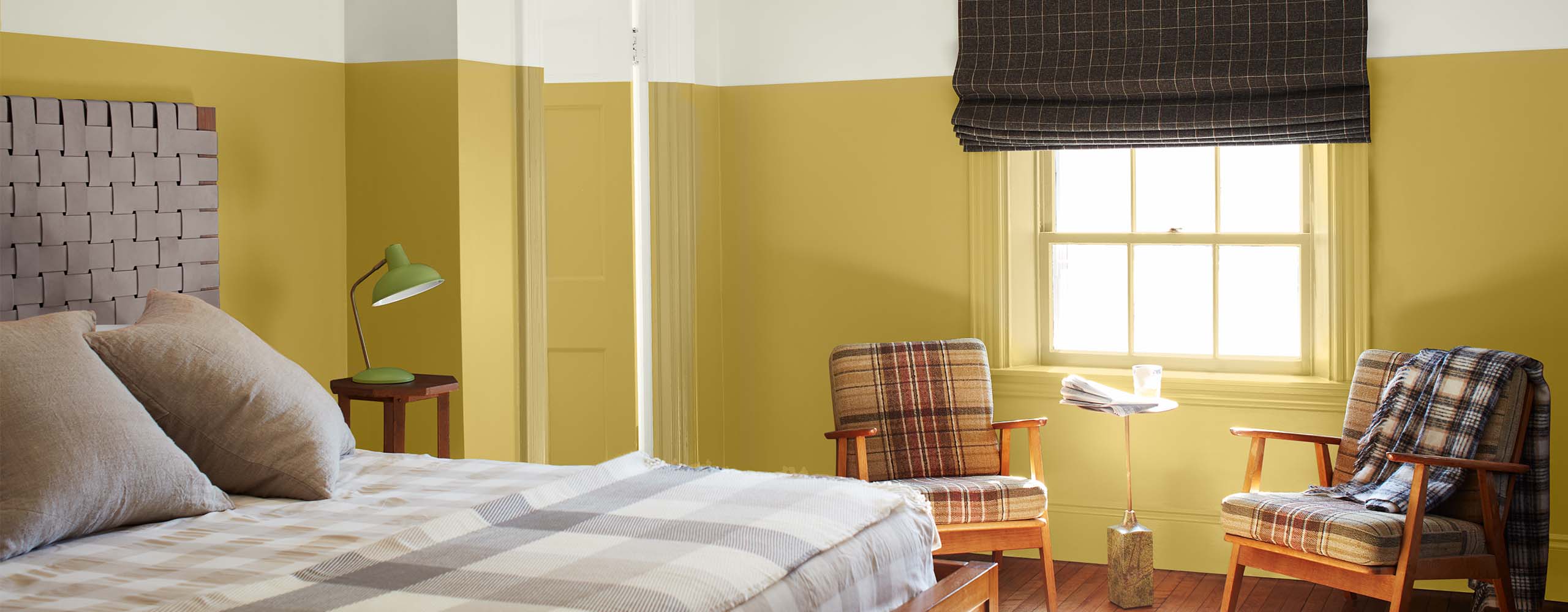 A bright two-tone painted bedroom with white-painted upper walls, upper door and ceiling, yellow-painted lower walls and door, tan checked bedding and two plaid chairs. A bright two-tone painted bedroom with white-painted upper walls, upper door and ceiling, yellow-painted lower walls and door, tan checked bedding and two plaid chairs.