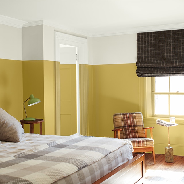 A bright two-tone painted bedroom with white-painted upper walls, upper door and ceiling, yellow-painted lower walls and door, tan checked bedding and two plaid chairs. A bright two-tone painted bedroom with white-painted upper walls, upper door and ceiling, yellow-painted lower walls and door, tan checked bedding and two plaid chairs.