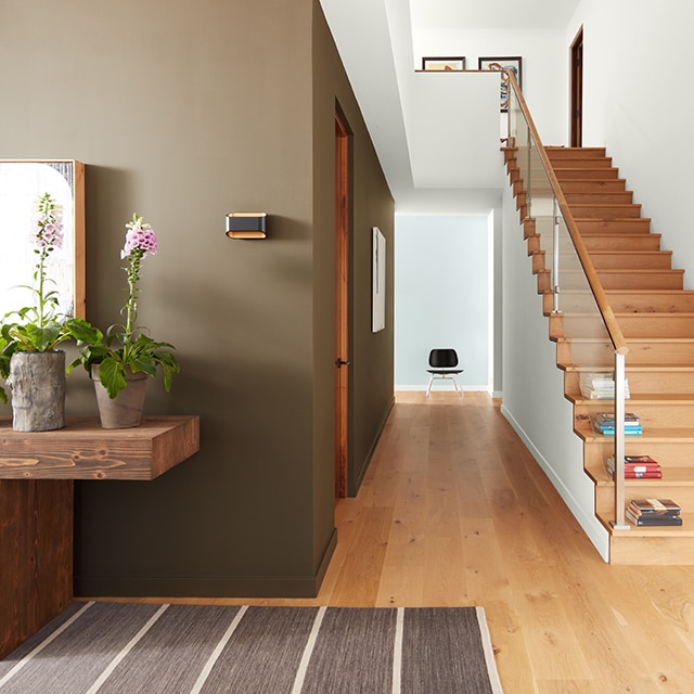 A brown-painted hallway, white ceiling, and wooden stairs leading to a white hallway; earthy natural decor. A brown-painted hallway, white ceiling, and wooden stairs leading to a white hallway; earthy natural decor.