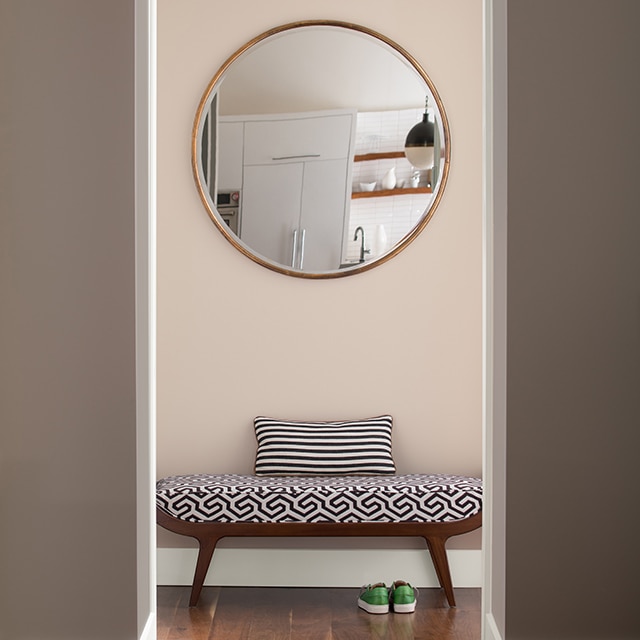 A contemporary hallway in light pink paint, and greige walls, with a modern bench, and circular wall mirror. A contemporary hallway in light pink paint, and greige walls, with a modern bench, and circular wall mirror.