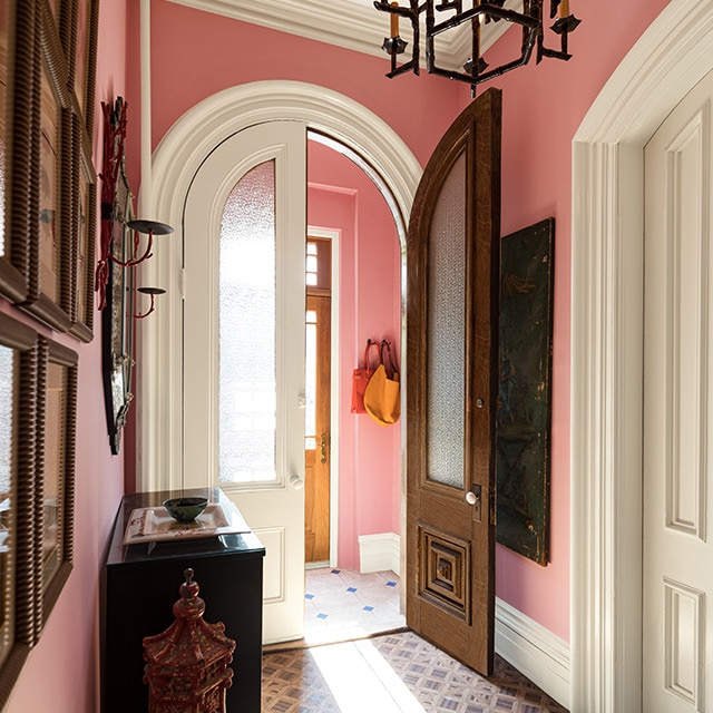 A traditional hallway and vestibule with pink-painted walls, white trim, doors, and ceiling, a bureau and chandelier. A traditional hallway and vestibule with pink-painted walls, white trim, doors, and ceiling, a bureau and chandelier.