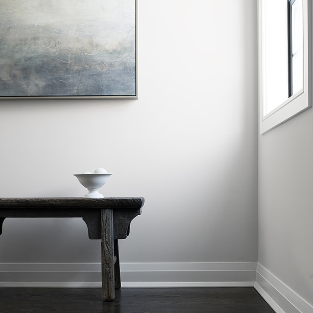 A hallway with white walls and trim, a black wooden bench, and contemporary art. A hallway with white walls and trim, a black wooden bench, and contemporary art.