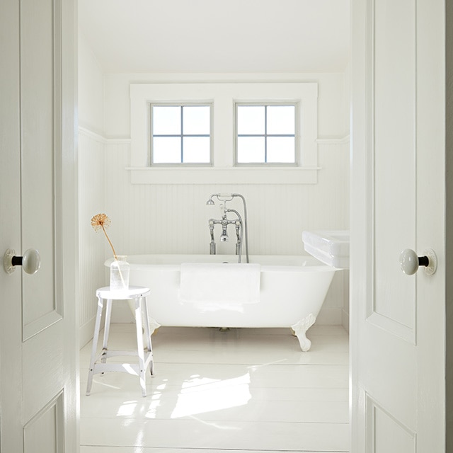 An all-white painted bathroom with two white-trimmed windows over a clawfoot tub and white-painted doors and ceiling. An all-white painted bathroom with two white-trimmed windows over a clawfoot tub and white-painted doors and ceiling.