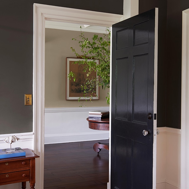 A room with soft black painted upper walls and white lower walls with white trim and an open black door leading to a hallway in neutral hues. A room with soft black painted upper walls and white lower walls with white trim and an open black door leading to a hallway in neutral hues.