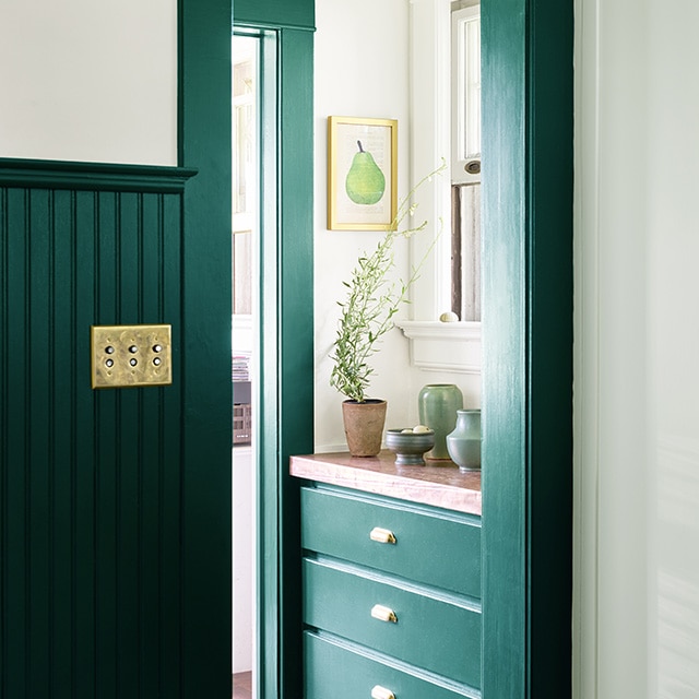 A hallway entrance with rich, dark green painted wainscoting, trim and built-in drawers underneath a window, and pale green painted wall cabinets. A hallway entrance with rich, dark green painted wainscoting, trim and built-in drawers underneath a window, and pale green painted wall cabinets.