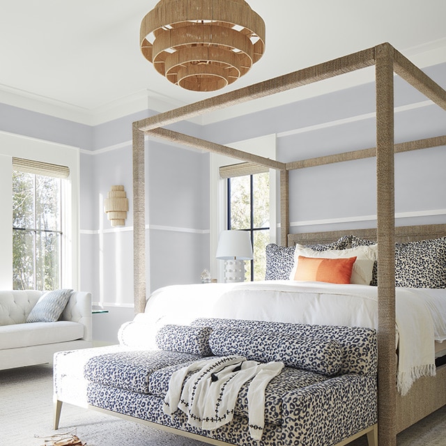 A bright and airy light-gray painted bedroom with white wall trim and ceiling, a modern four-poster bed, a fun cheetah animal print sofa, and wicker chandelier. A bright and airy light-gray painted bedroom with white wall trim and ceiling, a modern four-poster bed, a fun cheetah animal print sofa, and wicker chandelier.