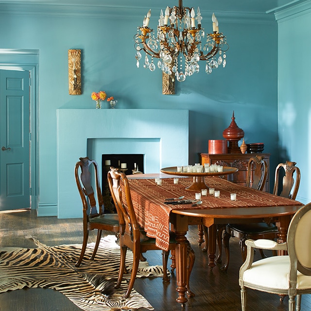 An opulent dining room with blue-painted walls, ceiling and fireplace, and a chandelier over a large wooden dining table and chairs. The style is classic with an exotic twist. An opulent dining room with blue-painted walls, ceiling and fireplace, and a chandelier over a large wooden dining table and chairs. The style is classic with an exotic twist.