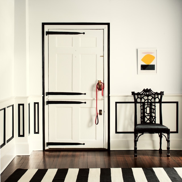 This black-and-white styled room features white-painted walls, ceiling and door with black trim and black decorative hinges on the door, a black chair and black-and-white striped rug. This black-and-white styled room features white-painted walls, ceiling and door with black trim and black decorative hinges on the door, a black chair and black-and-white striped rug.