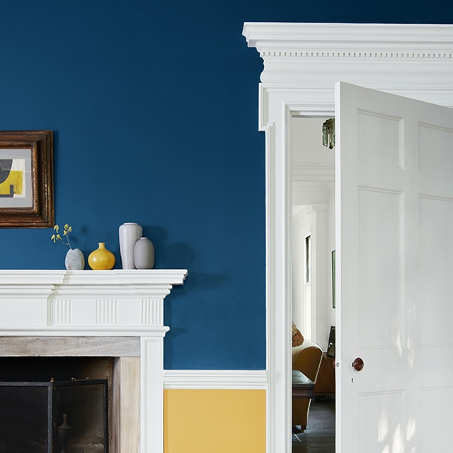 A striking two-tone painted living room wall with navy blue on the top, yellow on the bottom, beautiful white trim and molding, fireplace mantel and open door. A striking two-tone painted living room wall with navy blue on the top, yellow on the bottom, beautiful white trim and molding, fireplace mantel and open door.