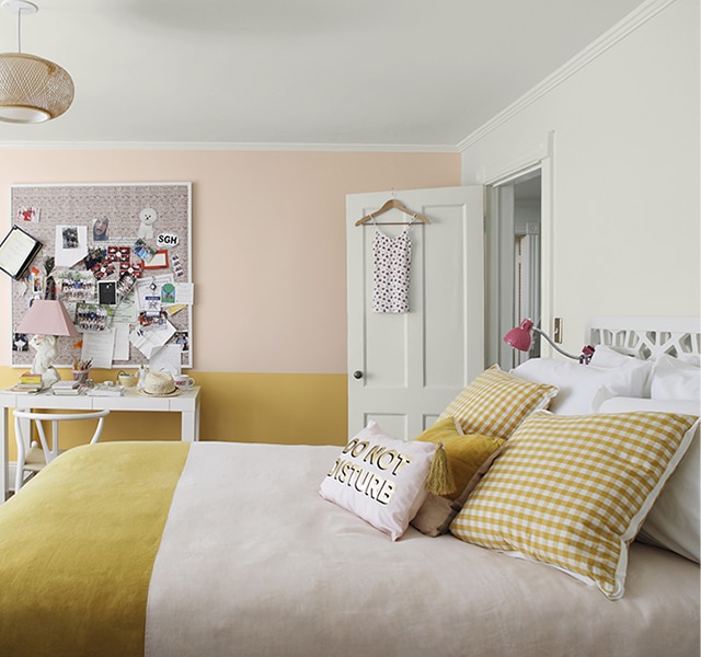 Chambre d’un blanc apaisant avec mur d’accent rose pâle en haut et jaune en bas, literie assortie à deux tons, table et chaise blanches, babillard et fauteuil poire. Chambre d’un blanc apaisant avec mur d’accent rose pâle en haut et jaune en bas, literie assortie à deux tons, table et chaise blanches, babillard et fauteuil poire.