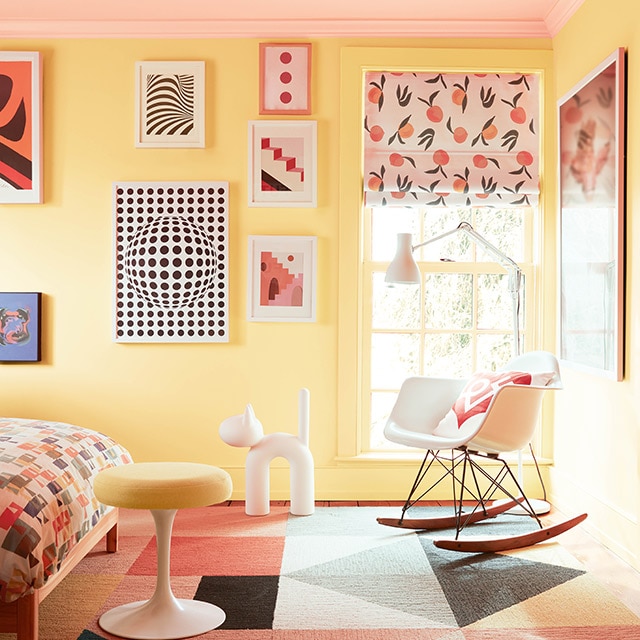 Chambre d’enfant lumineuse et riante avec murs jaunes, plafond rose pâle, œuvres d’art colorées, mobilier moderne, couvre-lit multicolore et tapis aux motifs géométriques. Chambre d’enfant lumineuse et riante avec murs jaunes, plafond rose pâle, œuvres d’art colorées, mobilier moderne, couvre-lit multicolore et tapis aux motifs géométriques.