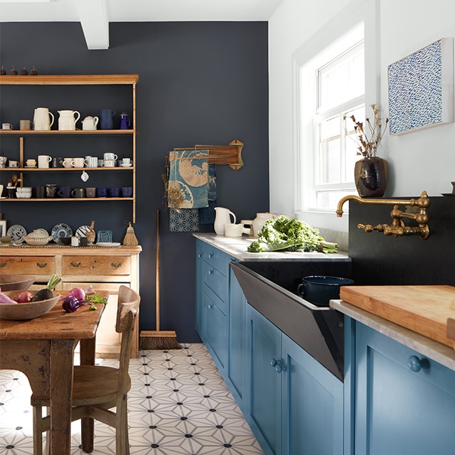 An English heritage-style kitchen with blue-painted cabinets, an accent wall painted in navy, and wood furniture. An English heritage-style kitchen with blue-painted cabinets, an accent wall painted in navy, and wood furniture.