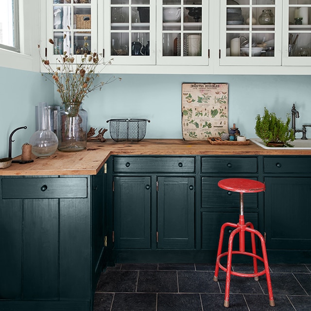 A modern farmhouse kitchen with light blue painted walls, white cabinets, dark green-painted lower cabinets and a red stool. A modern farmhouse kitchen with light blue painted walls, white cabinets, dark green-painted lower cabinets and a red stool.