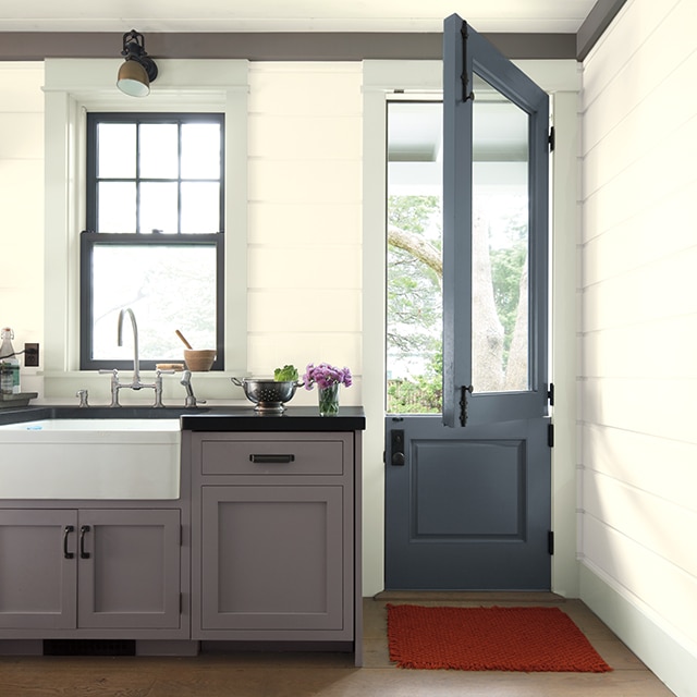 A charming kitchen with white-painted shiplap walls and ceiling, gray cabinets and crown molding, an open blue Dutch door, and wood floor. A charming kitchen with white-painted shiplap walls and ceiling, gray cabinets and crown molding, an open blue Dutch door, and wood floor.