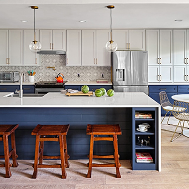 The same kitchen after a makeover, with white-painted upper cabinets, dark blue lower cabinets and island, white countertops, and a small dining set. The same kitchen after a makeover, with white-painted upper cabinets, dark blue lower cabinets and island, white countertops, and a small dining set.