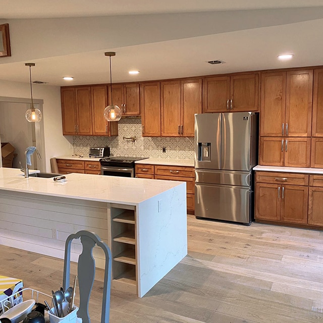 A bright, open kitchen with wood cabinets on one wall, and a large white island with a sink before a makeover. A bright, open kitchen with wood cabinets on one wall, and a large white island with a sink before a makeover.