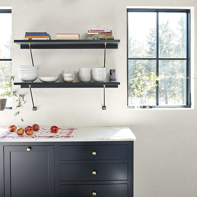 A pretty sunlit kitchen with dark navy-painted cabinets and floating shelves, a white wall, and natural wood beamed ceiling. A pretty sunlit kitchen with dark navy-painted cabinets and floating shelves, a white wall, and natural wood beamed ceiling.