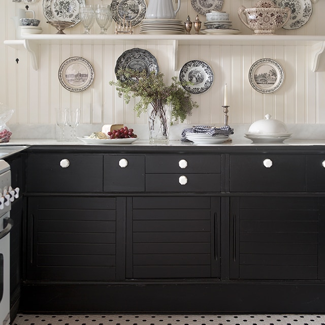 A white-painted French country kitchen with open shelving and patterned plates above black-painted cabinets, and a black and white tile floor. A white-painted French country kitchen with open shelving and patterned plates above black-painted cabinets, and a black and white tile floor.