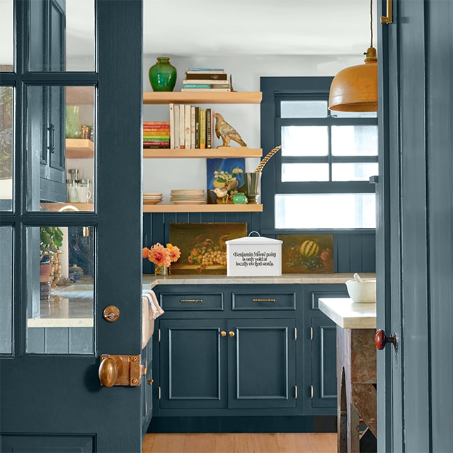 Pretty teal-painted doors open to a kitchen with teal cabinets, trim and backsplash, and floating wood shelves against a light gray wall. Pretty teal-painted doors open to a kitchen with teal cabinets, trim and backsplash, and floating wood shelves against a light gray wall.
