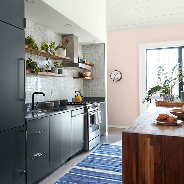 A welcoming small kitchen with charcoal gray-painted cabinets, pearl gray tile backsplash, a pink accent wall and blue striped area rug. A welcoming small kitchen with charcoal gray-painted cabinets, pearl gray tile backsplash, a pink accent wall and blue striped area rug.