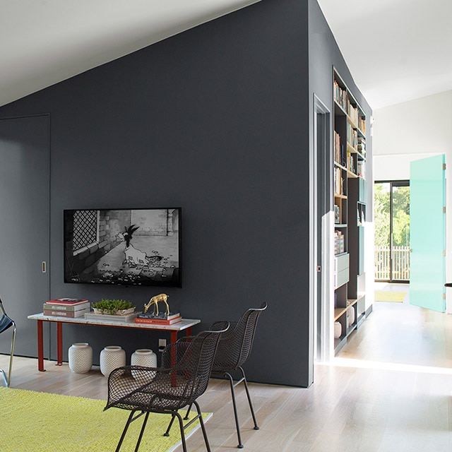 A bright, open living room area with black accent walls and door, a white vaulted ceiling and walls, modern furniture, and a light blue door at the end of a hallway. A bright, open living room area with black accent walls and door, a white vaulted ceiling and walls, modern furniture, and a light blue door at the end of a hallway.