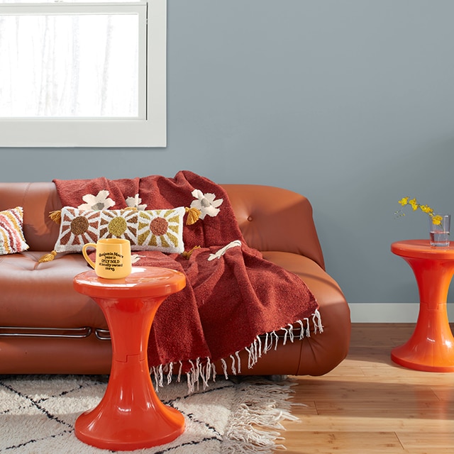 A fun, retro-style living room with a blue-gray painted wall, white trim, a brown leather couch, and two orange tables. A fun, retro-style living room with a blue-gray painted wall, white trim, a brown leather couch, and two orange tables.