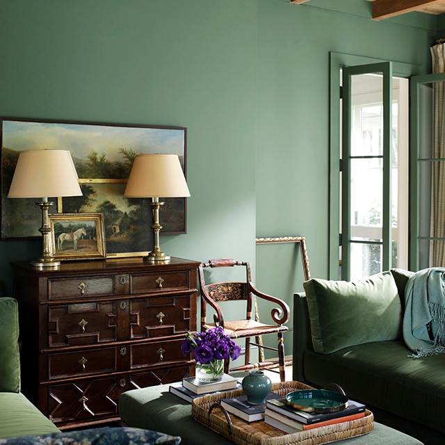 An elegant and relaxing monochromatic living room with rich, green painted walls and open French doors, green velvet sofas, a wood bureau with lamps, and wood beamed ceiling. An elegant and relaxing monochromatic living room with rich, green painted walls and open French doors, green velvet sofas, a wood bureau with lamps, and wood beamed ceiling.