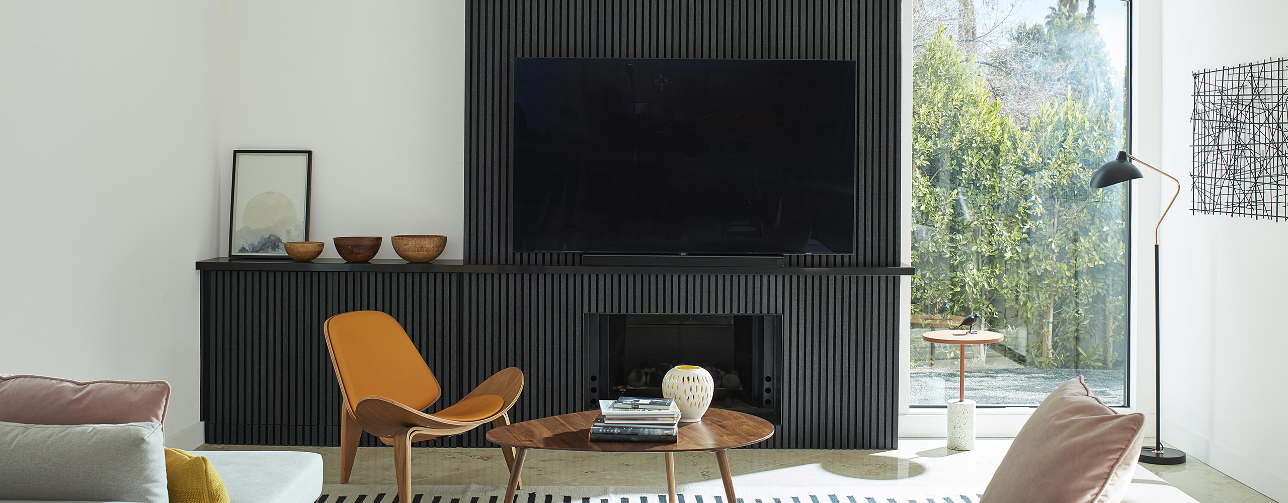 A mid-century modern style living room with bright, white-painted walls and vaulted ceiling, and a black paneled accent wall, built-in cabinet and fireplace, and large screen tv. A mid-century modern style living room with bright, white-painted walls and vaulted ceiling, and a black paneled accent wall, built-in cabinet and fireplace, and large screen tv.