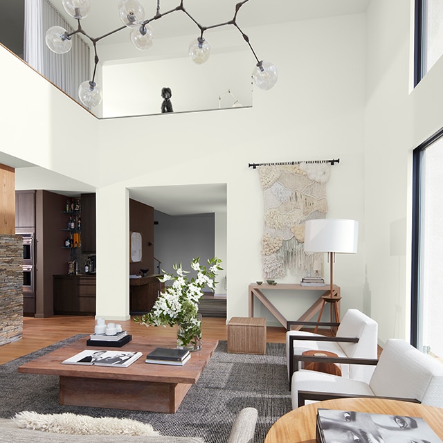 A bright open, white-painted mezzanine style living room with modern white and wood furnishings, a hanging light fixture, and dark brown and gray far walls. A bright open, white-painted mezzanine style living room with modern white and wood furnishings, a hanging light fixture, and dark brown and gray far walls.