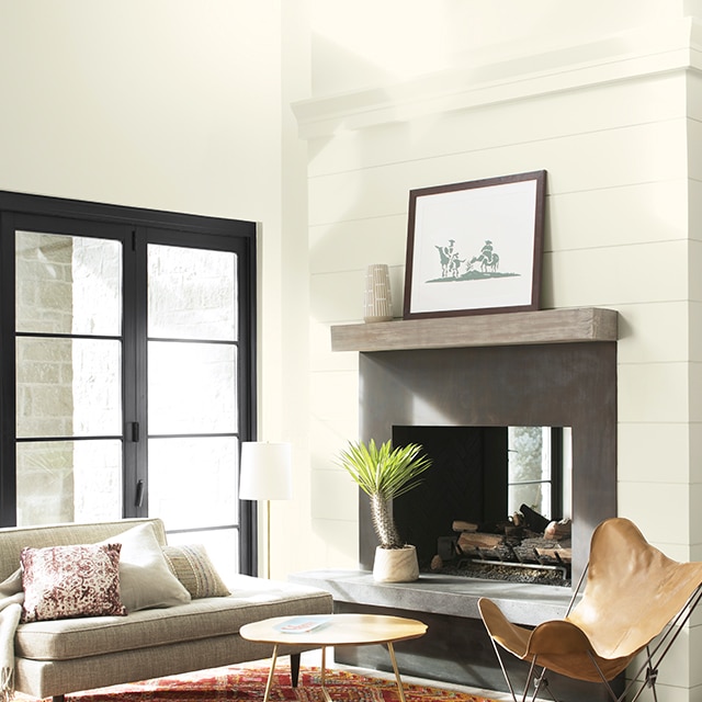A white-painted living room with vaulted ceiling, fireplace, modern furniture, layered orange and red area rugs, and black French doors. A white-painted living room with vaulted ceiling, fireplace, modern furniture, layered orange and red area rugs, and black French doors.