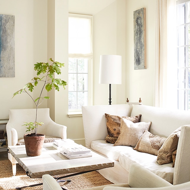 An inviting, sunlit, white-painted living room with a comfy white sofa and two chairs, and a stone top table with a potted plant. An inviting, sunlit, white-painted living room with a comfy white sofa and two chairs, and a stone top table with a potted plant.