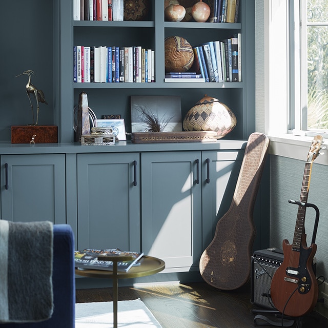 Sunlight reflecting on beautiful gray-blue painted built-in shelves and cabinets in a home office, with a guitar, amp, and case against the lower right wall. Sunlight reflecting on beautiful gray-blue painted built-in shelves and cabinets in a home office, with a guitar, amp, and case against the lower right wall.