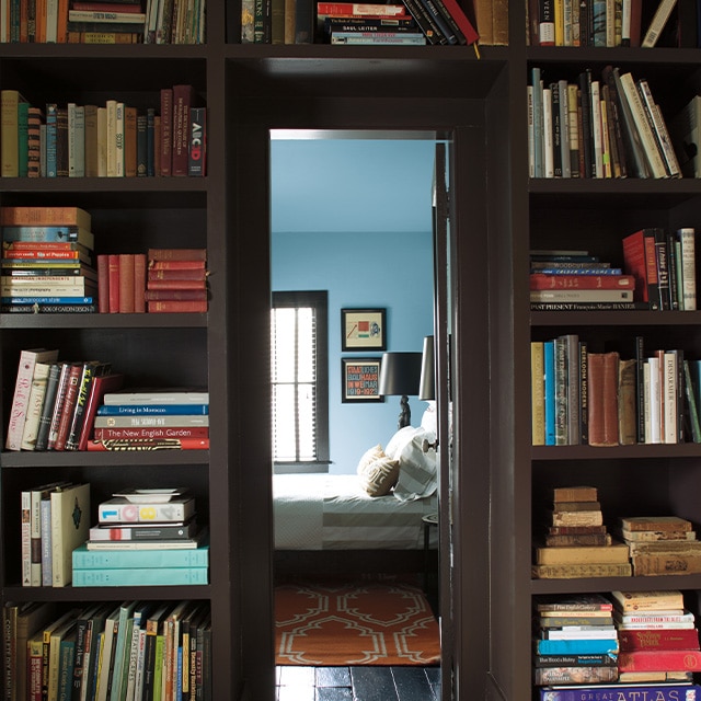 A doorway framed by dark brown painted built-in bookshelves open into a blue painted bedroom. A doorway framed by dark brown painted built-in bookshelves open into a blue painted bedroom.