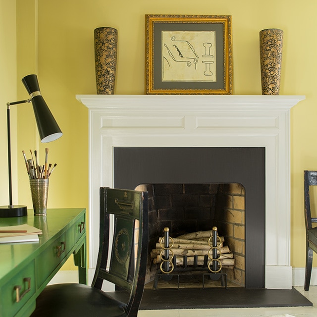 A pretty green desk and black chair contrast nicely in this yellow painted room with a white fireplace mantel, and black-and-white abstract rug. A pretty green desk and black chair contrast nicely in this yellow painted room with a white fireplace mantel, and black-and-white abstract rug.